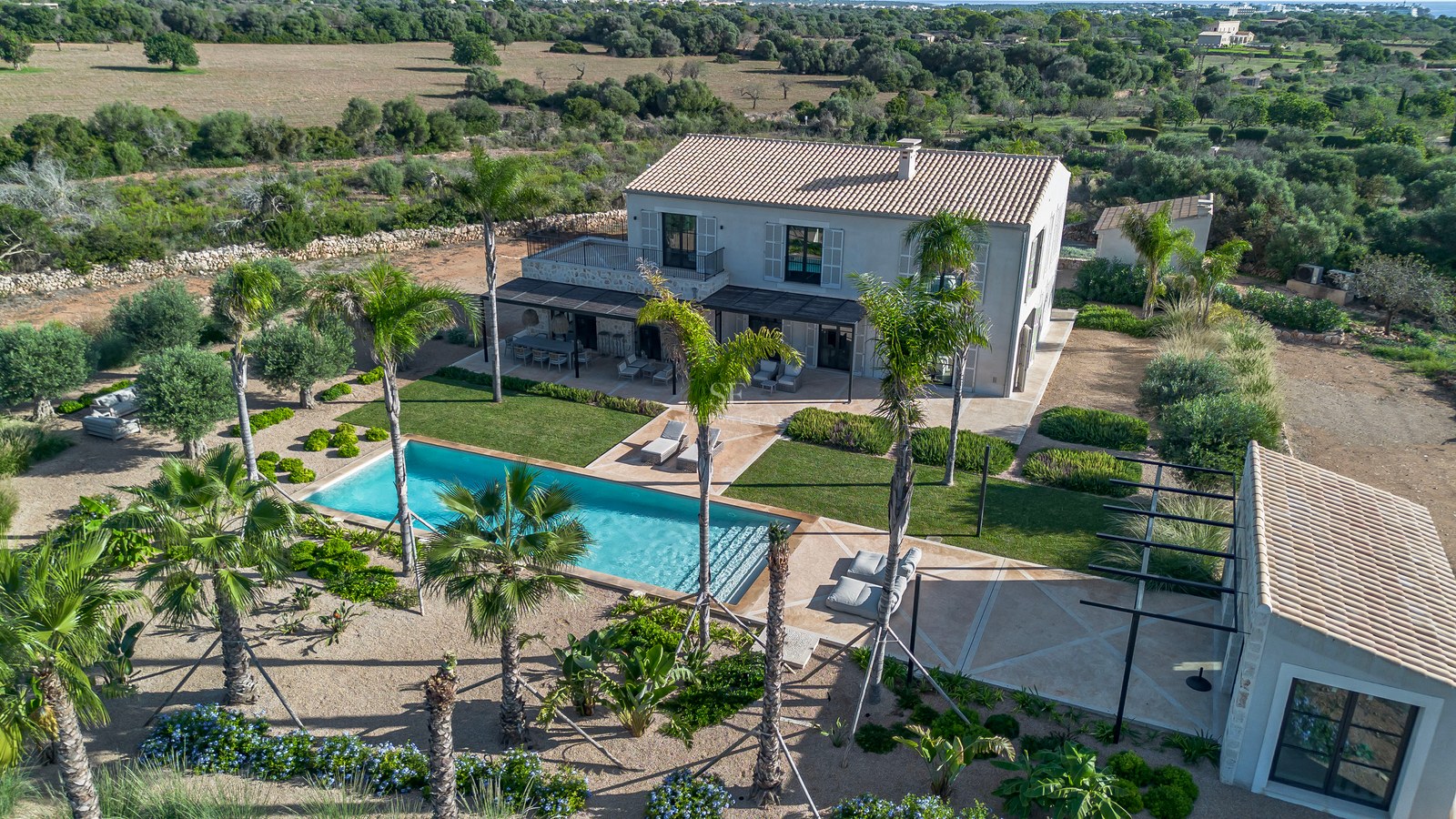 Vue aérienne d'une villa de luxe avec piscine turquoise, palmiers et jardins paysagers.