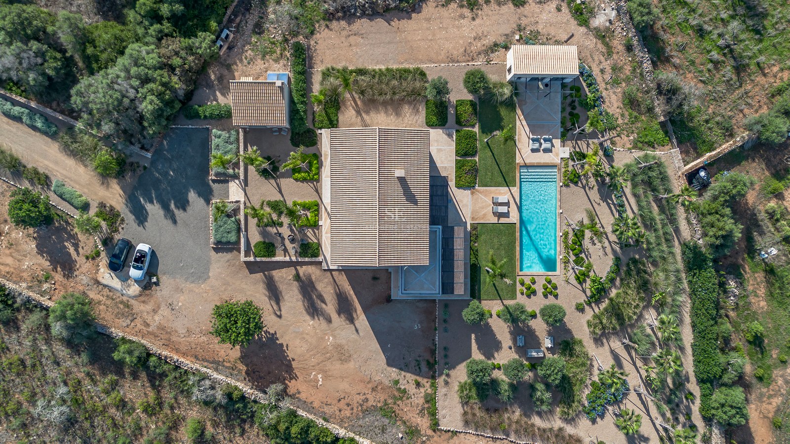 Vue à vol d'oiseau d'une villa moderne avec piscine turquoise, jardins paysagers et toits en terre cuite.