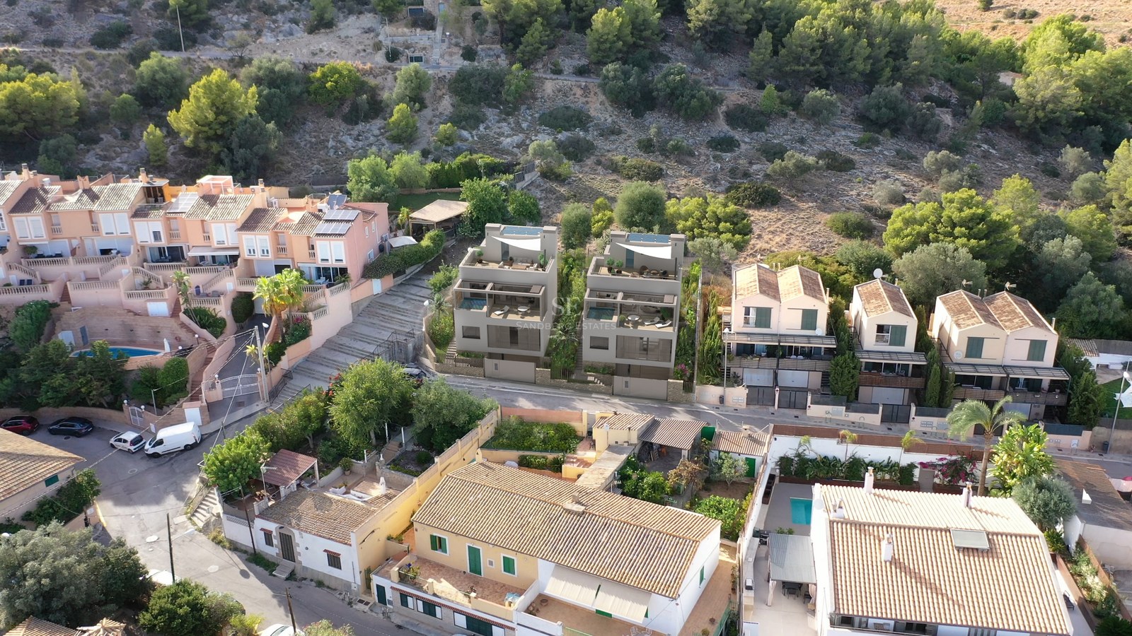 Vue aérienne de deux villas contemporaines grises entourées de maisons méditerranéennes traditionnelles en colline.