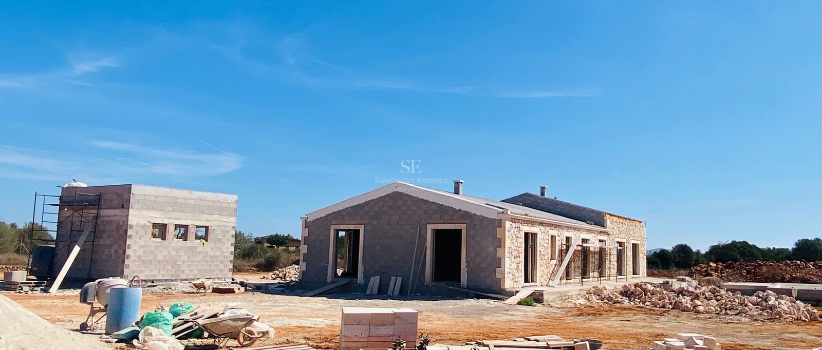 Construction site of a modern Mediterranean villa with natural stone cladding under a clear blue sky.