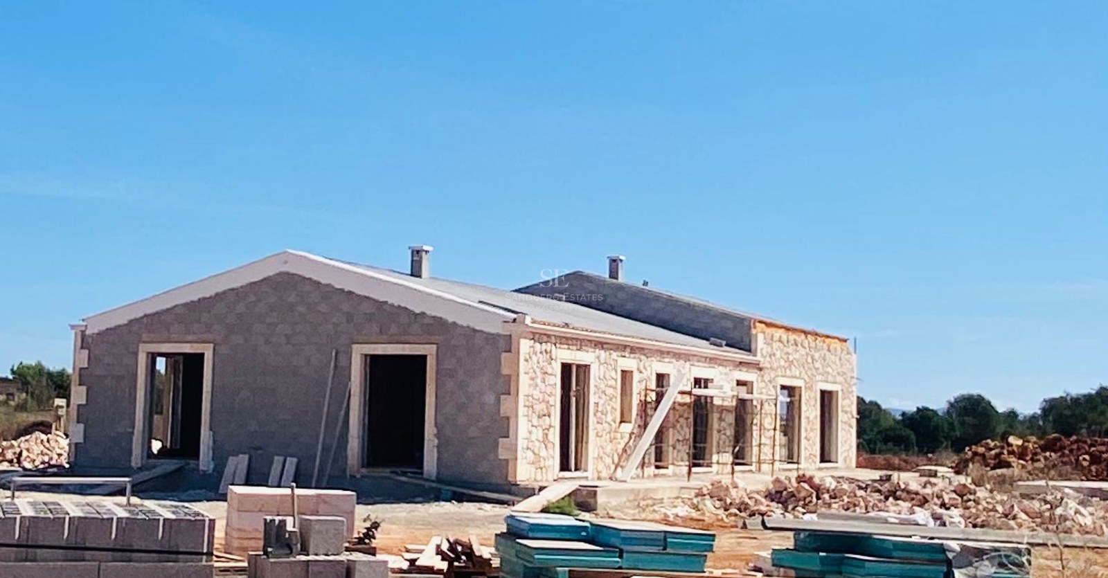Exterior view of a luxury Mediterranean villa with natural stone cladding under construction against a clear blue sky.