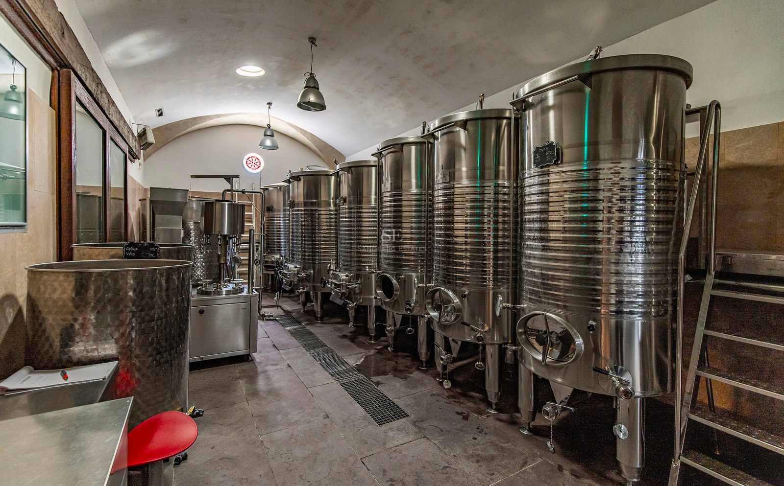 Rangée de cuves de fermentation en acier inoxydable sous un plafond voûté dans un domaine viticole privé.