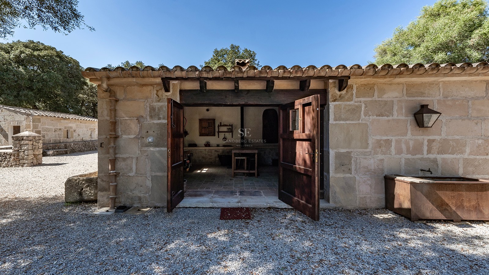 Vue extérieure d'un bâtiment traditionnel en pierre avec portes en bois ouvertes et cour en gravier.