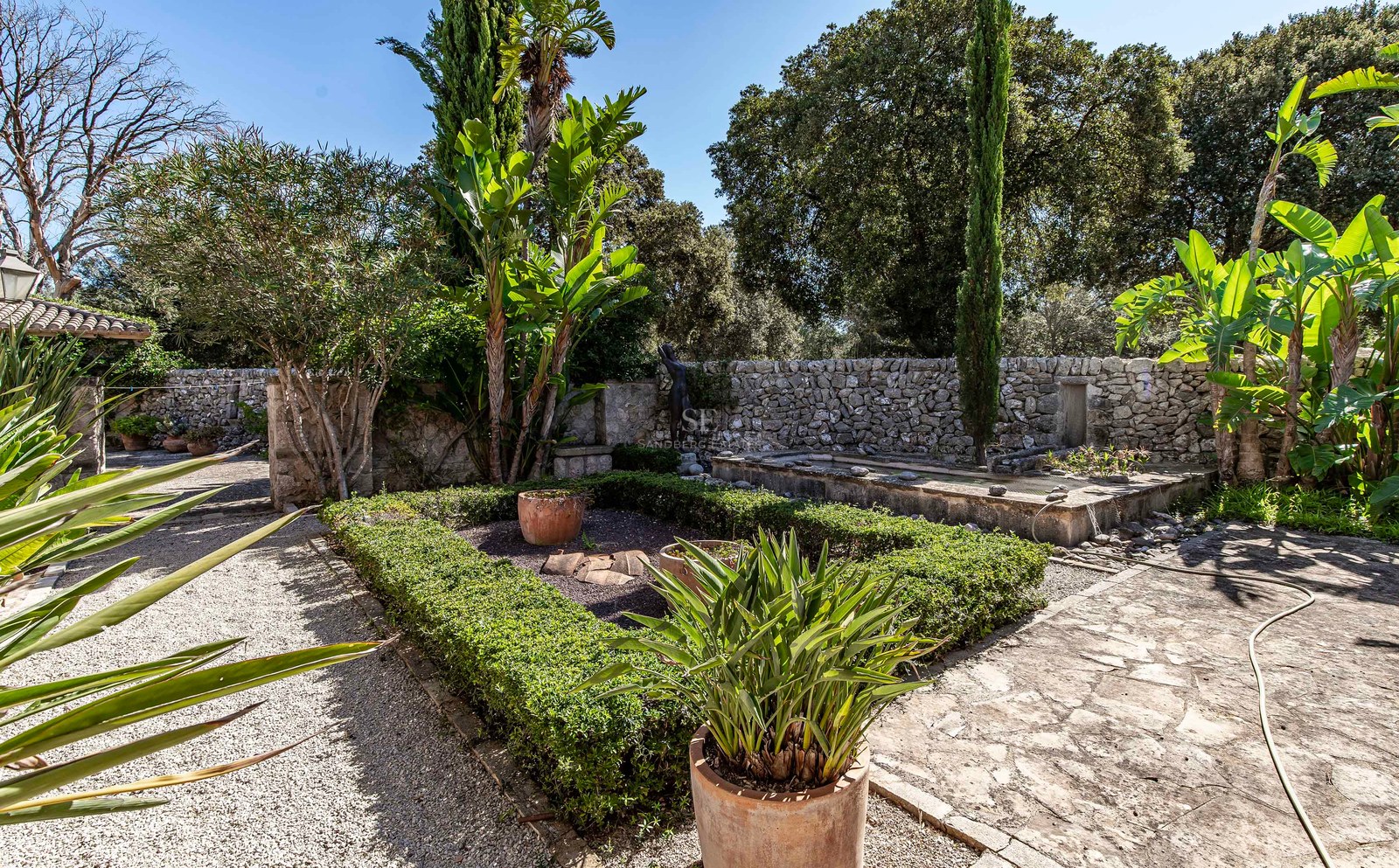 Jardin méditerranéen avec murs en pierre sèche, haies taillées, pots en terre cuite et allées de gravier.