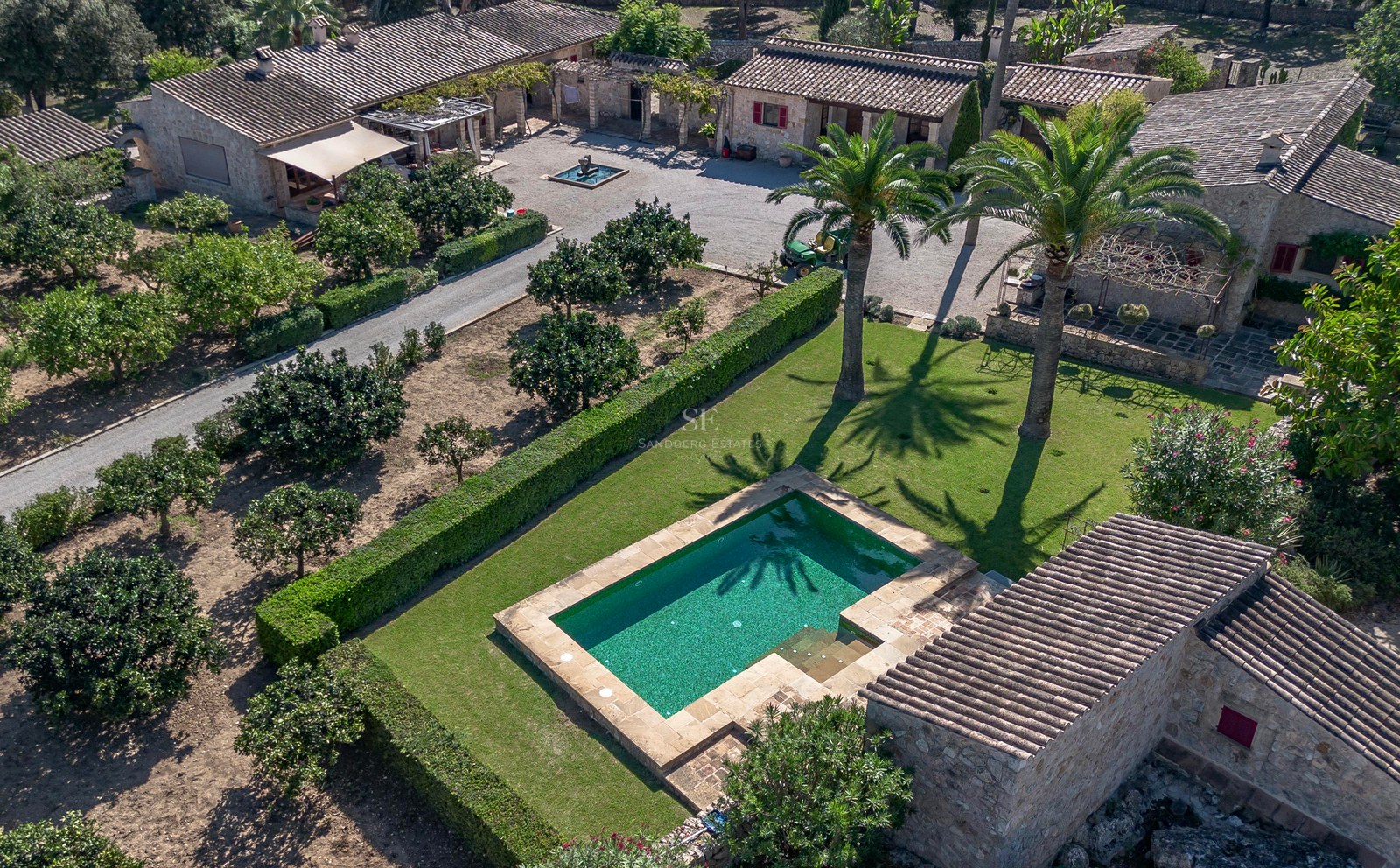 Vue aérienne d'une finca rustique en pierre avec piscine, palmiers et vastes jardins paysagers.