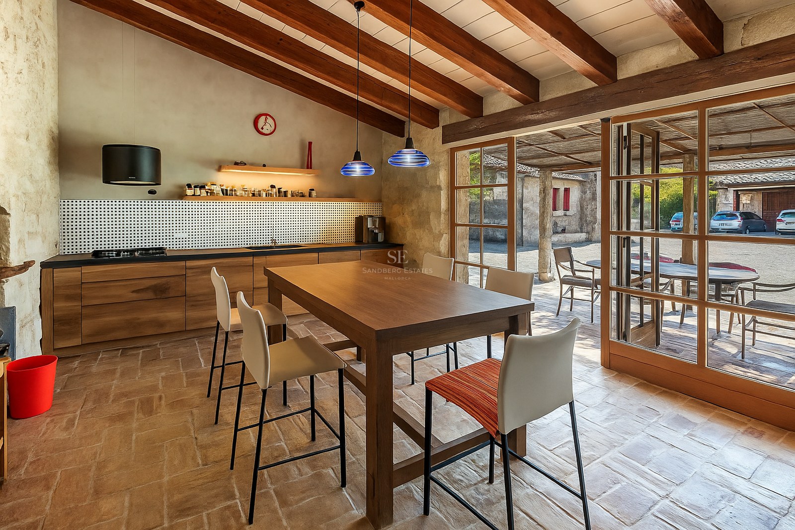 Cuisine avec poutres apparentes, sol en terre cuite et grandes portes vitrées ouvrant sur l'extérieur.