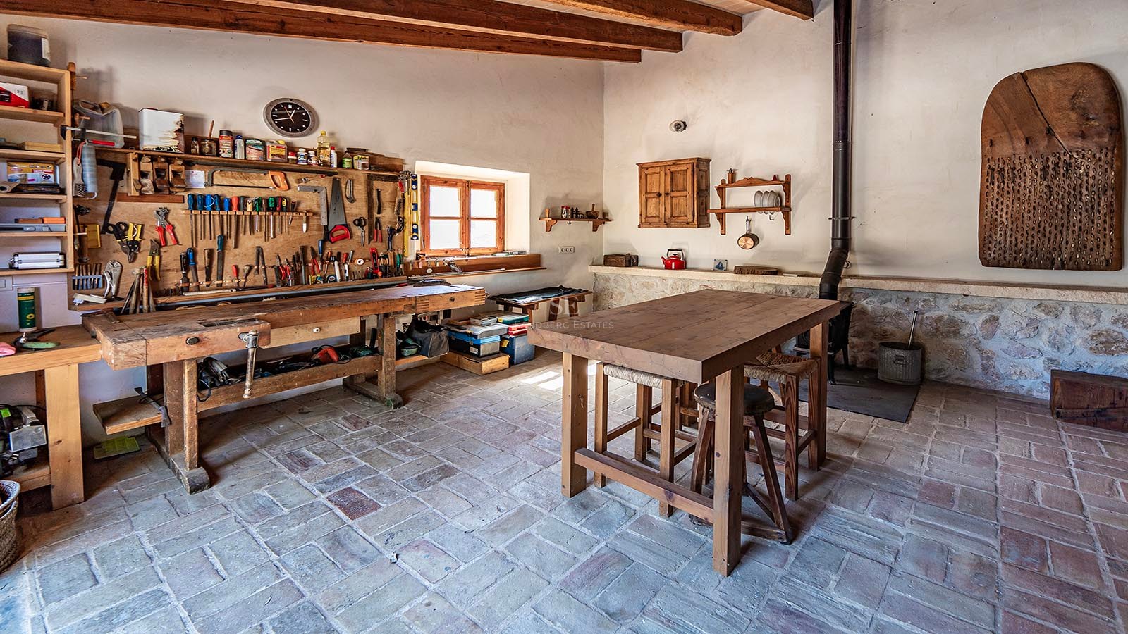 Atelier traditionnel avec un grand établi en bois, des outils au mur et des sols en pierre rustique.