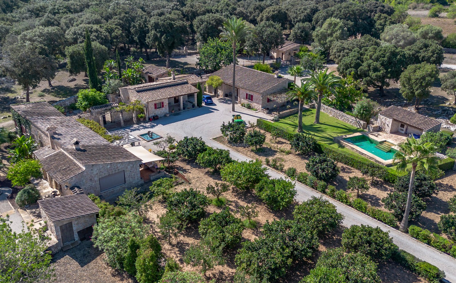 Vue aérienne d'un domaine en pierre avec plusieurs bâtiments, une piscine et de vastes vergers à Majorque.