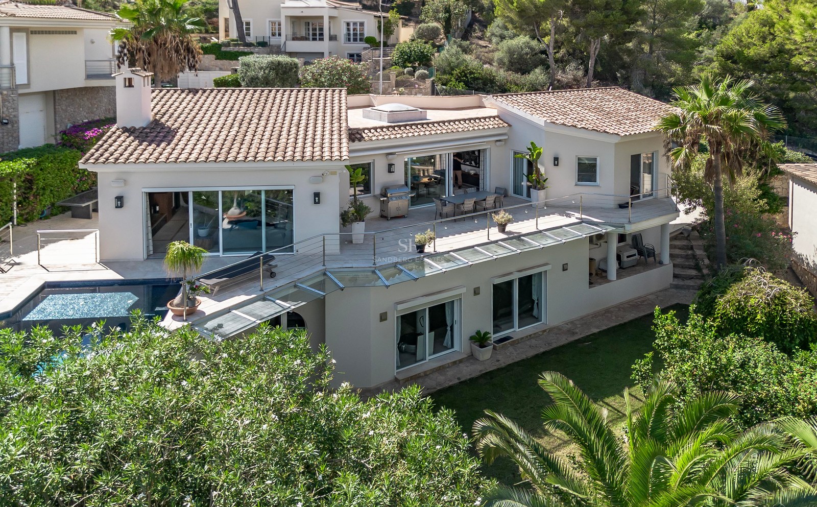 Vue aérienne d'une villa blanche à toit de tuiles, garde-corps en verre, grandes terrasses et piscine privée.