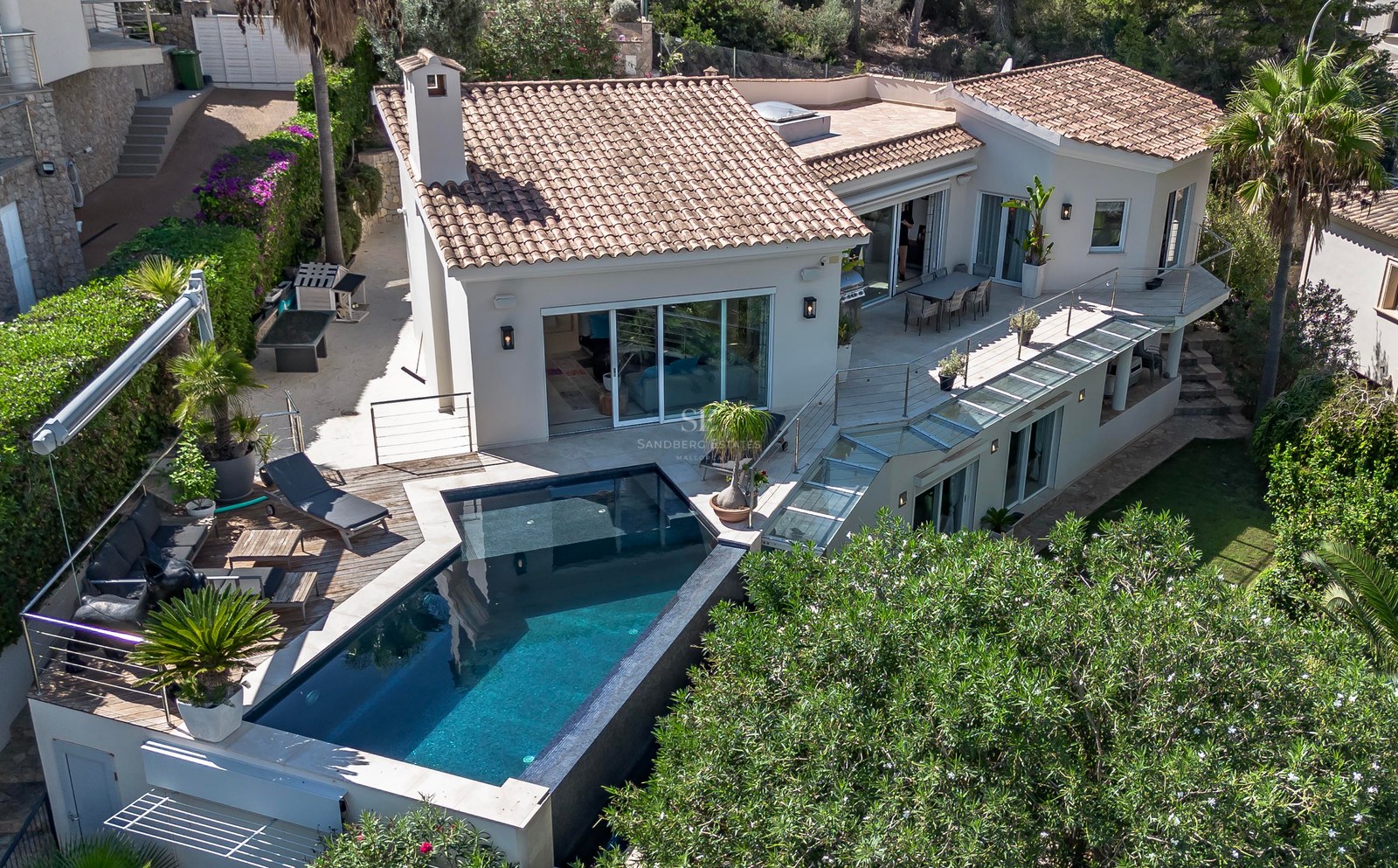 Vue aérienne d'une villa de luxe avec piscine carrelée sombre, terrasse en bois et paliers multiples.