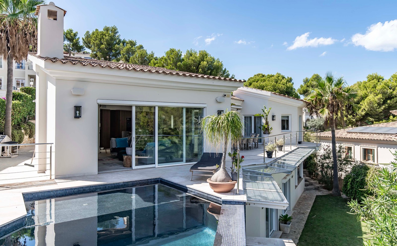 Vue en plongée d'une villa contemporaine blanche avec piscine carrelée sombre, terrasse vitrée et jardins luxuriants.