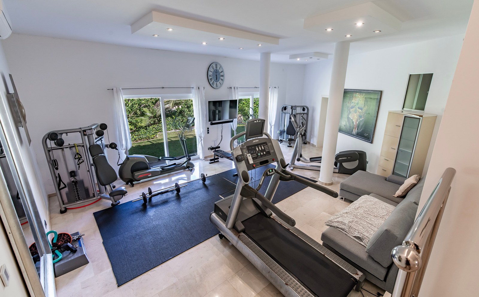 Salle de fitness à domicile spacieuse avec équipement professionnel, sol en marbre et accès extérieur.