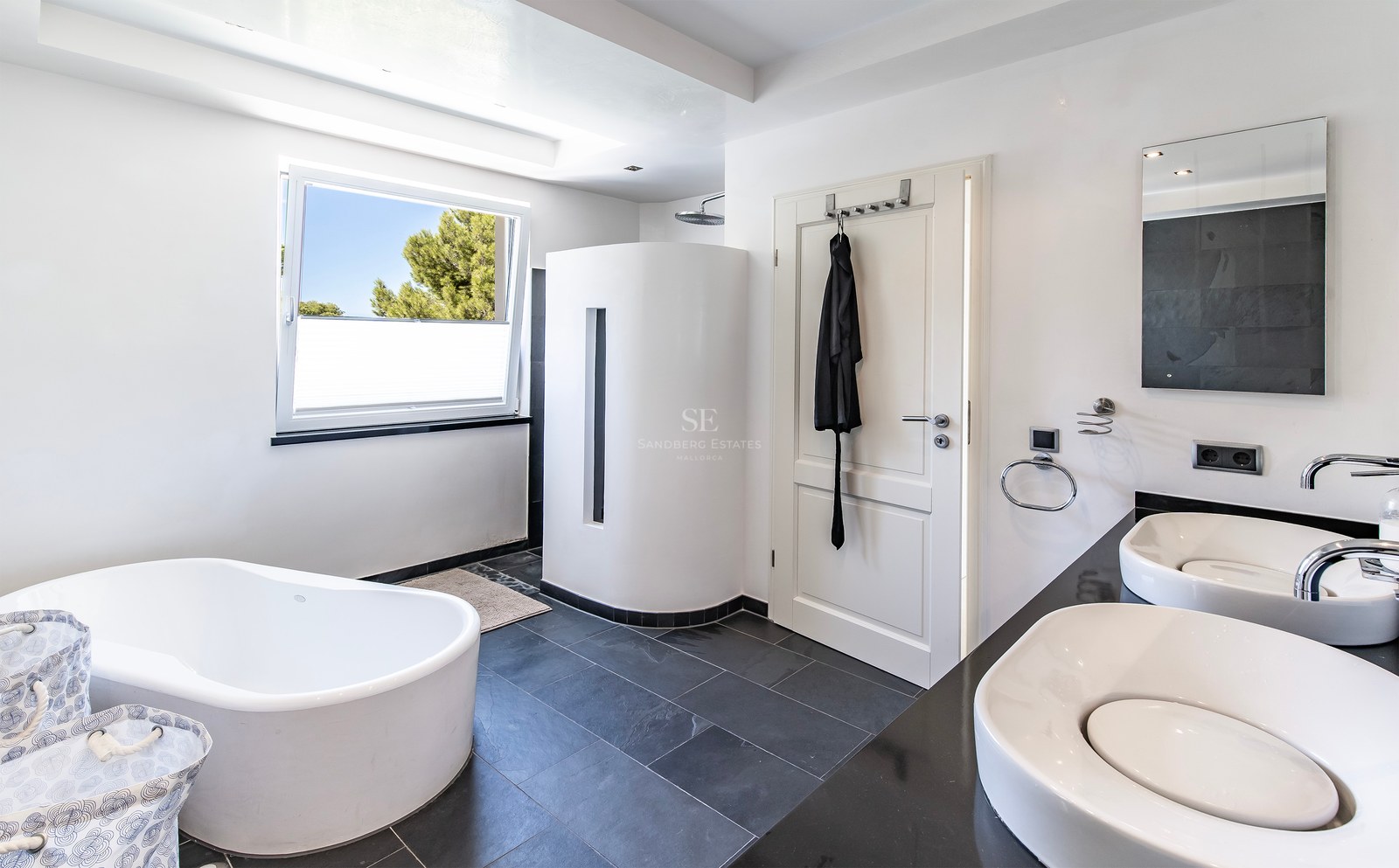 Salle de bains contemporaine avec baignoire en îlot, double vasque et sol en ardoise foncée.