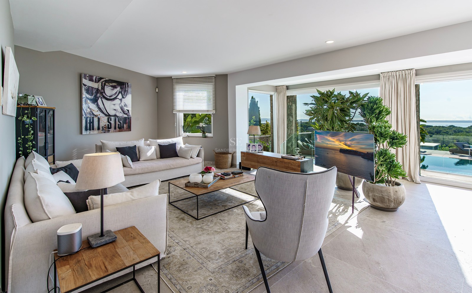 Salón moderno con sofás blancos, grandes ventanales con vistas a la piscina y al mar Mediterráneo.