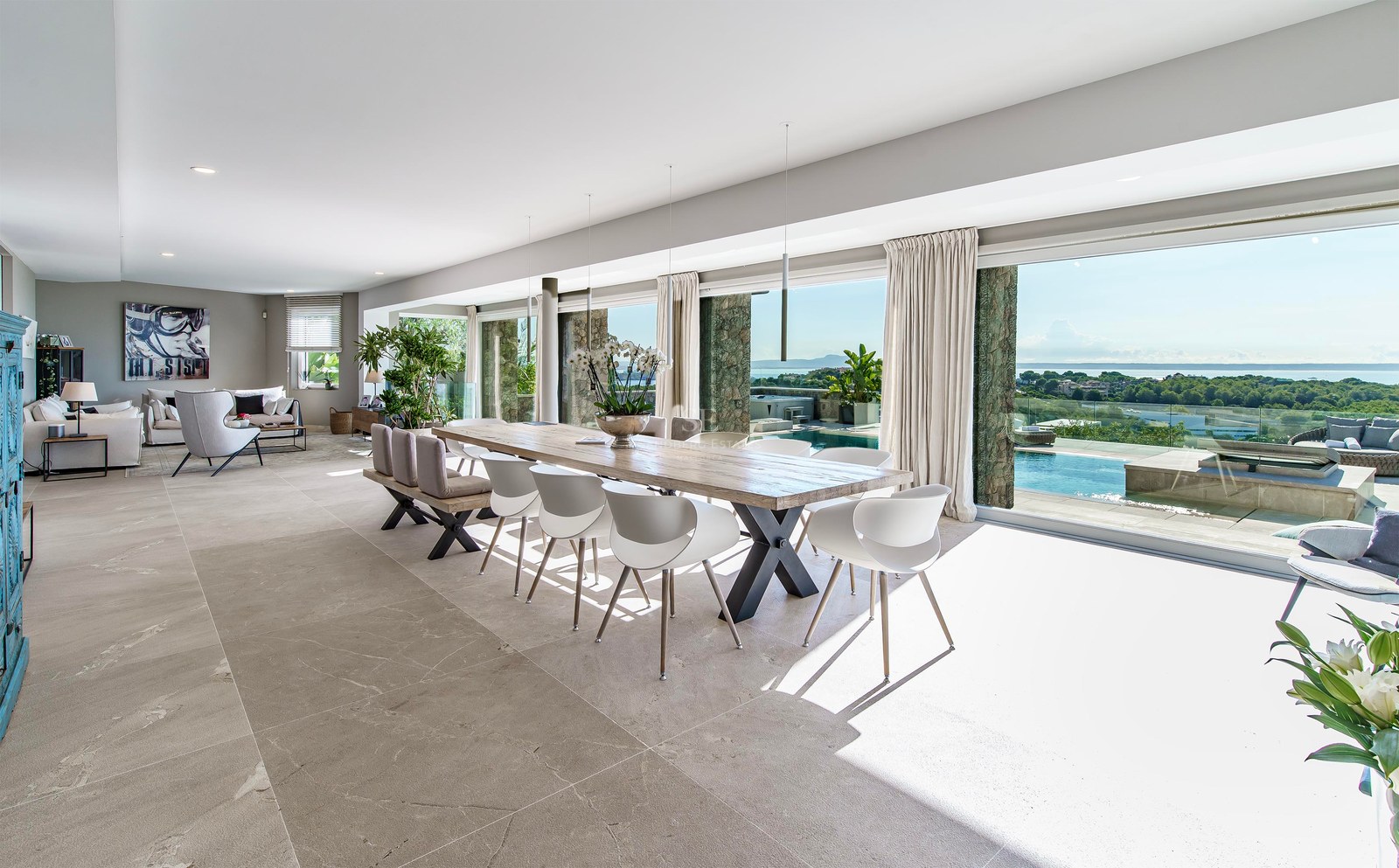 Comedor de planta abierta con mesa de madera y ventanales de suelo a techo con vistas a la piscina y al mar.