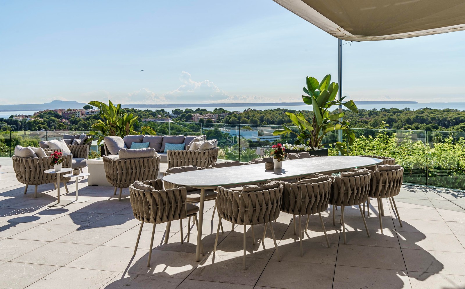 Terraza moderna con comedor, zona de estar, barandilla de cristal y vistas despejadas al mar y la costa.