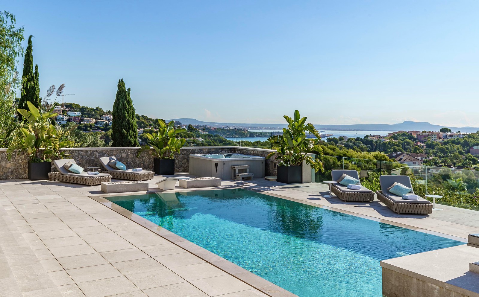 Piscina rectangular turquesa en terraza de piedra con jacuzzi y tumbonas frente al mar Mediterráneo.