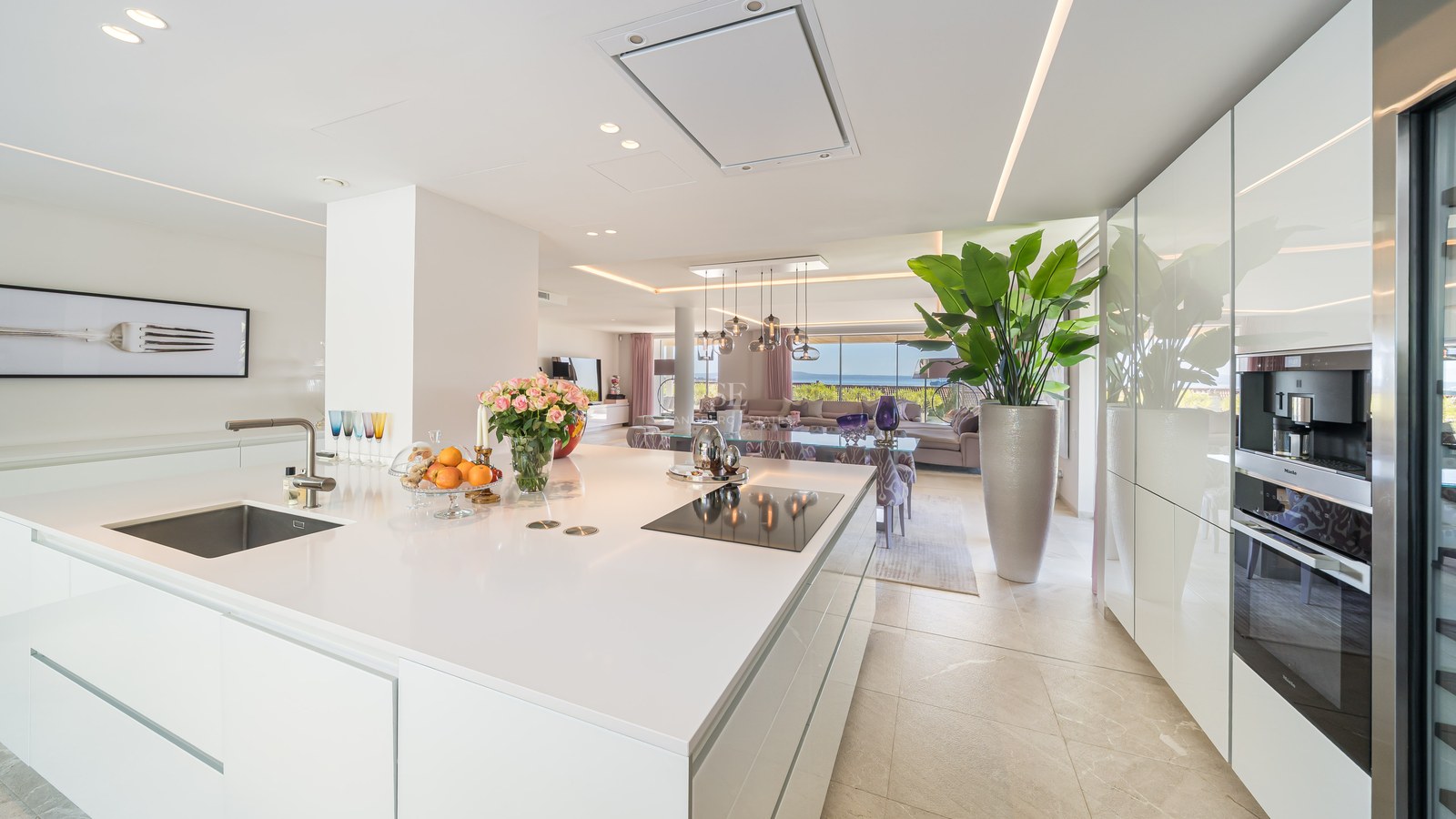 White kitchen island with induction hob, looking through to the living area and the Mediterranean sea beyond.