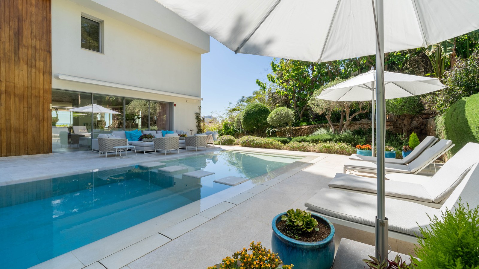 Modern rectangular swimming pool with stepping stones and white sun loungers on a natural stone terrace.