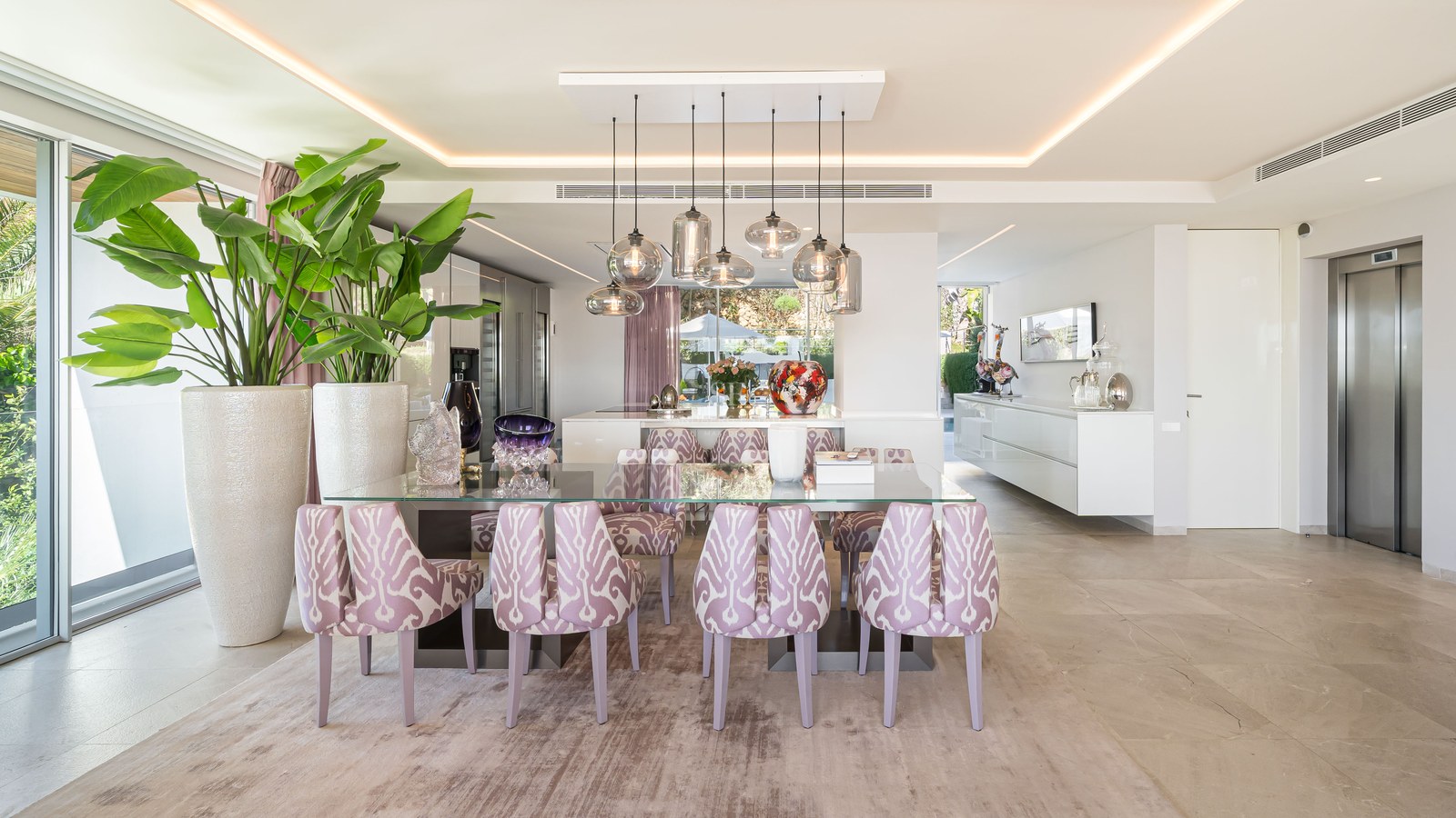 Contemporary dining room with a glass table, patterned lavender chairs, and designer glass pendant lighting.