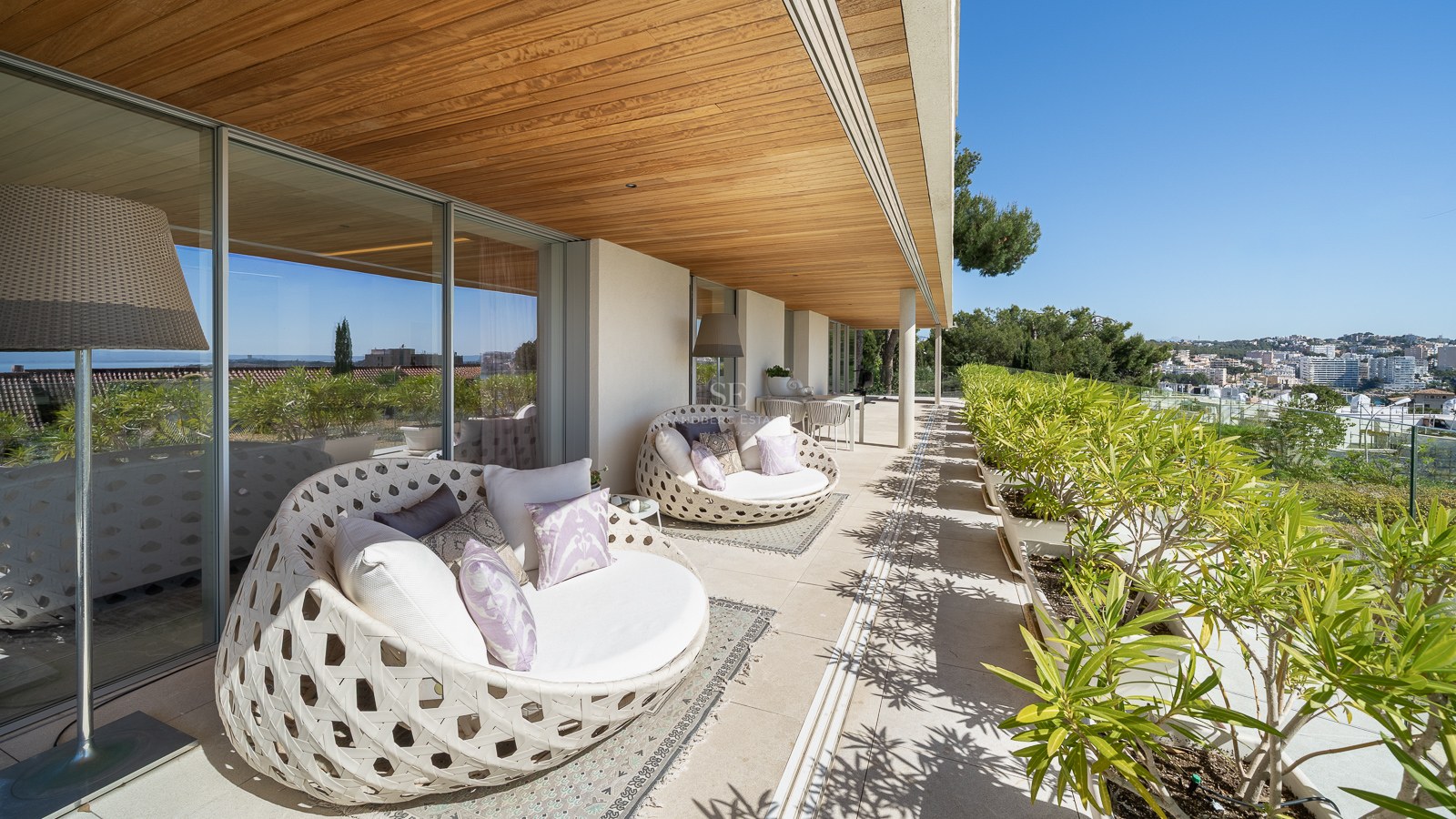 A long covered terrace featuring curved designer outdoor daybeds, wooden ceilings, and views over a Mediterranean town.