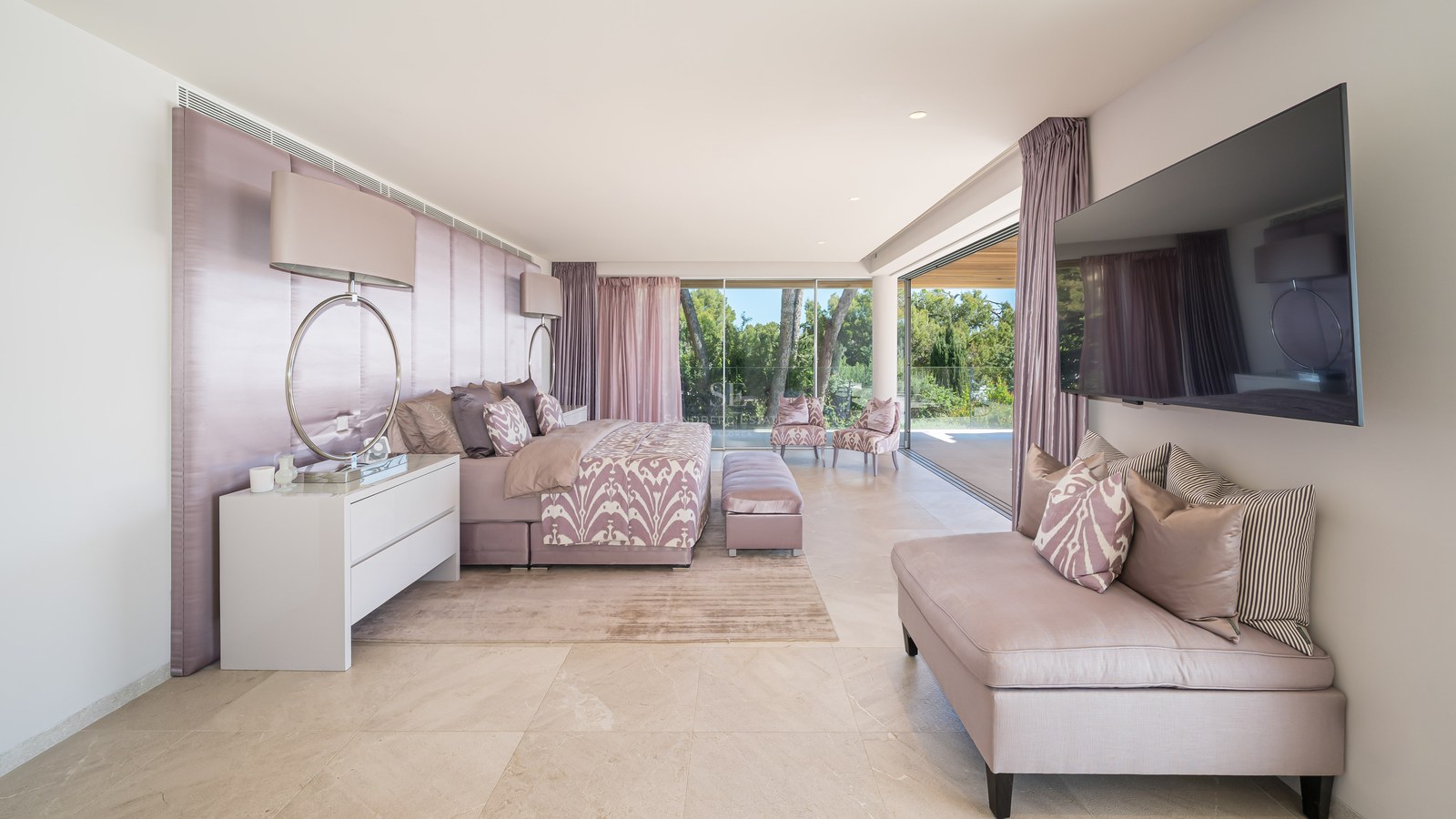 Spacious master bedroom featuring natural stone floors, a mauve upholstered headboard, and sliding doors to a terrace.