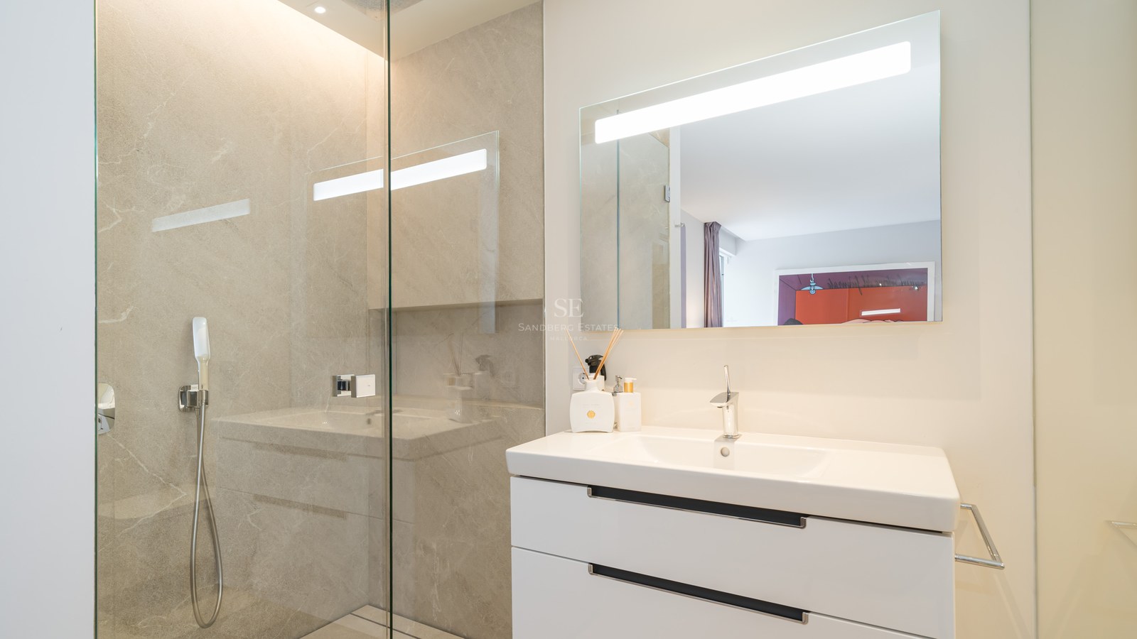 Modern bathroom featuring a glass walk-in shower, white floating vanity, and a large backlit LED mirror.