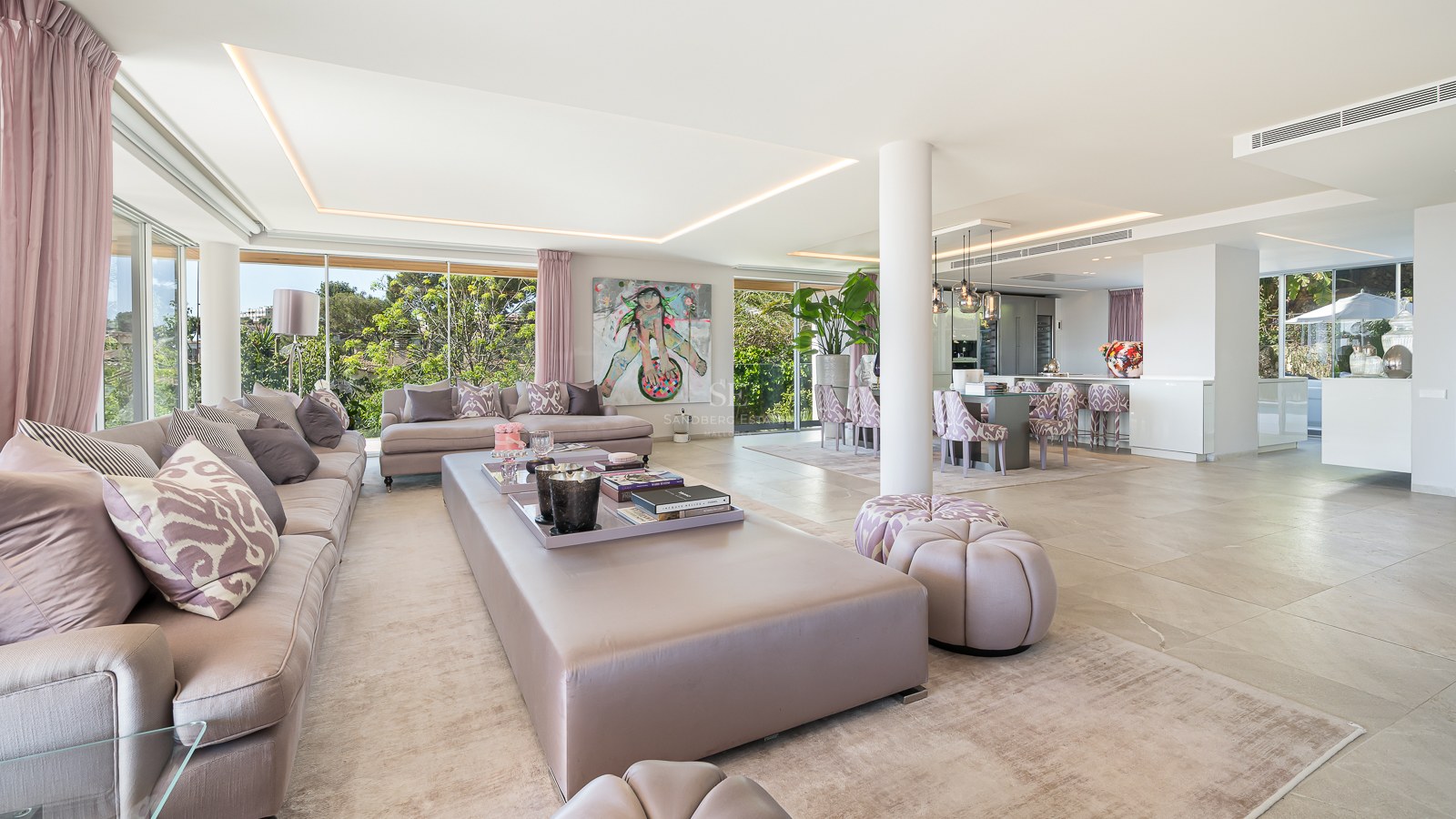 Spacious modern living room with plush grey sofas and floor-to-ceiling windows overlooking lush greenery.
