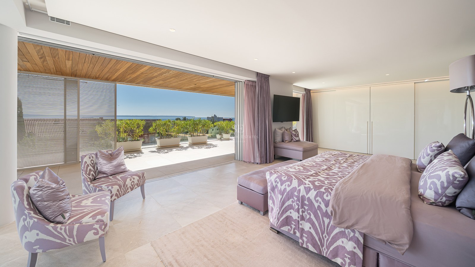 Spacious master bedroom with lavender accents opening onto a sun-drenched terrace with coastal views and wooden pergola.