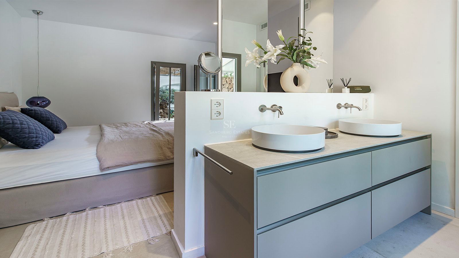 Dormitorio principal de planta abierta con tocador doble, dos lavabos sobre encimera y una cama grande con cojines azules.