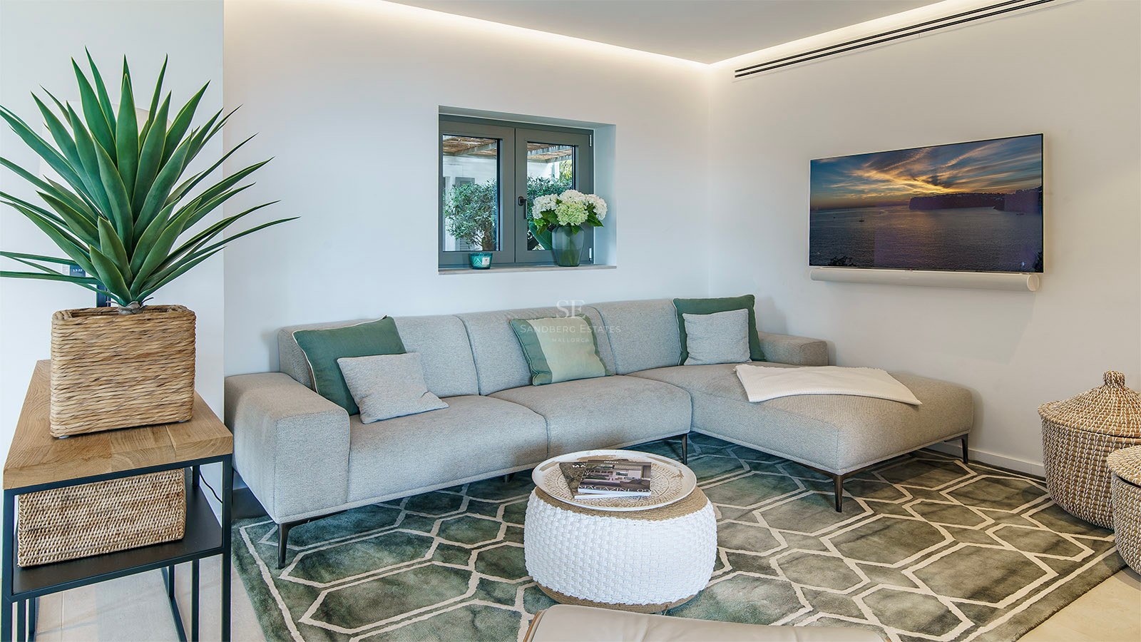 Interior de un salón contemporáneo con sofá gris, alfombra geométrica verde y televisión montada en la pared.