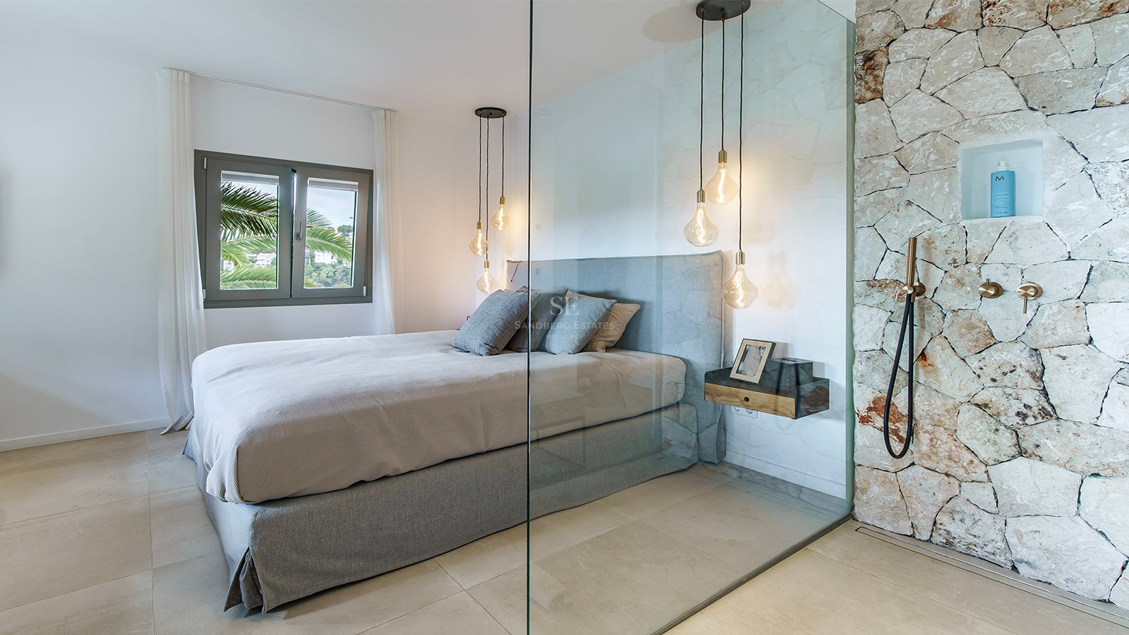 Dormitorio contemporáneo con cama gris, pared de cristal y ducha de piedra rústica con grifería de latón.