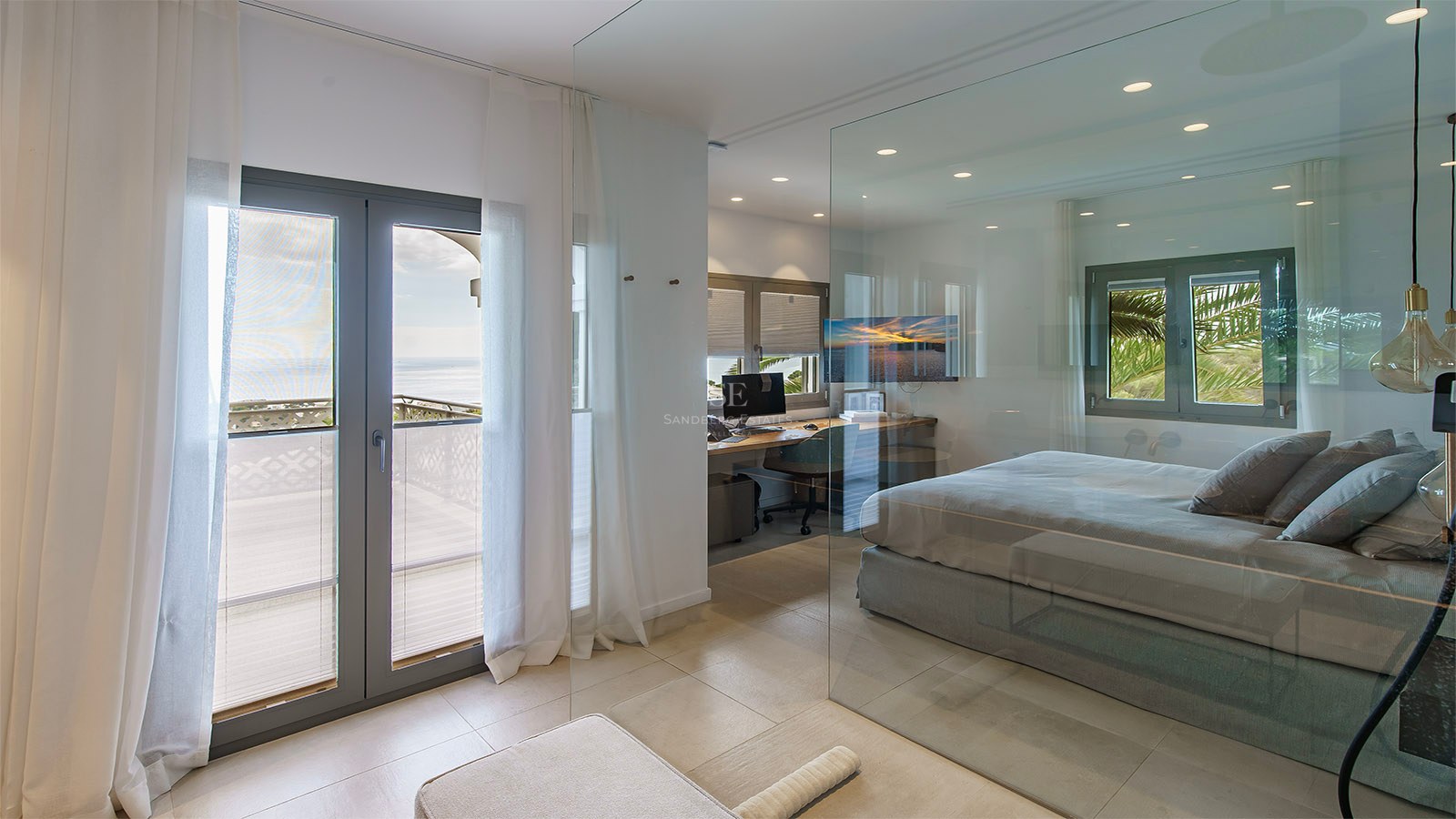 Dormitorio moderno con pared de cristal, zona de oficina integrada y balcón con vistas al mar.