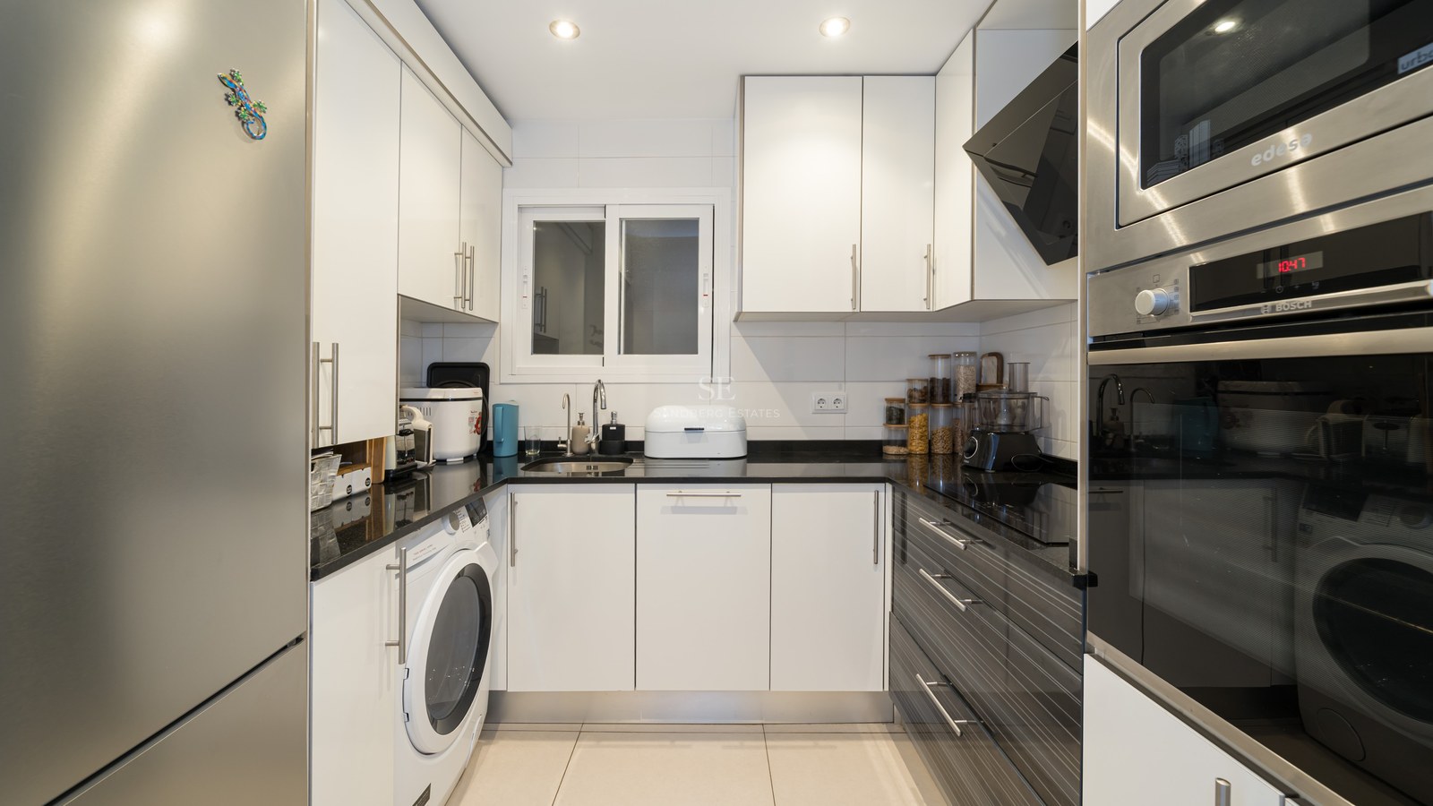 Cocina moderna en forma de U con armarios blancos, encimeras negras y electrodomésticos de acero inoxidable.