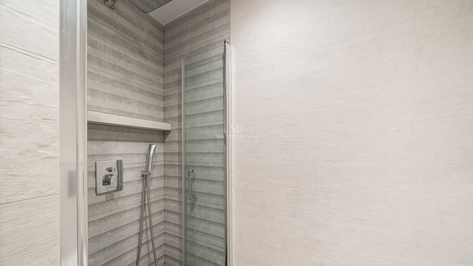 Ducha moderna con azulejos grises texturizados, puerta de cristal y grifería de cromo.