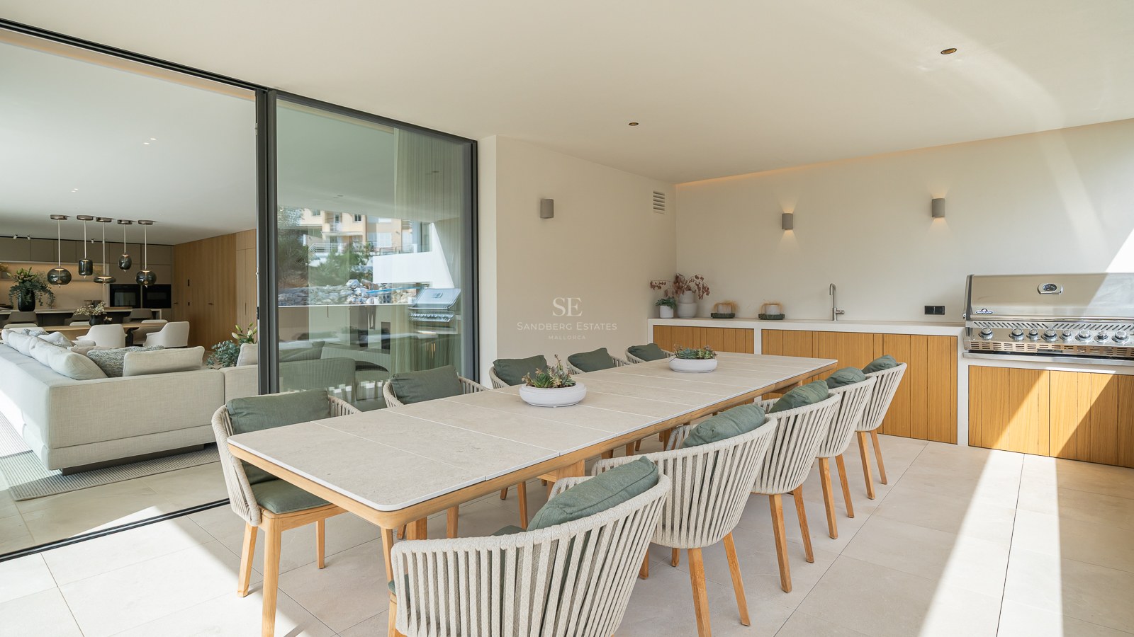 Grande table à manger extérieure avec dix chaises à côté d'une cuisine d'été professionnelle sur une terrasse couverte.