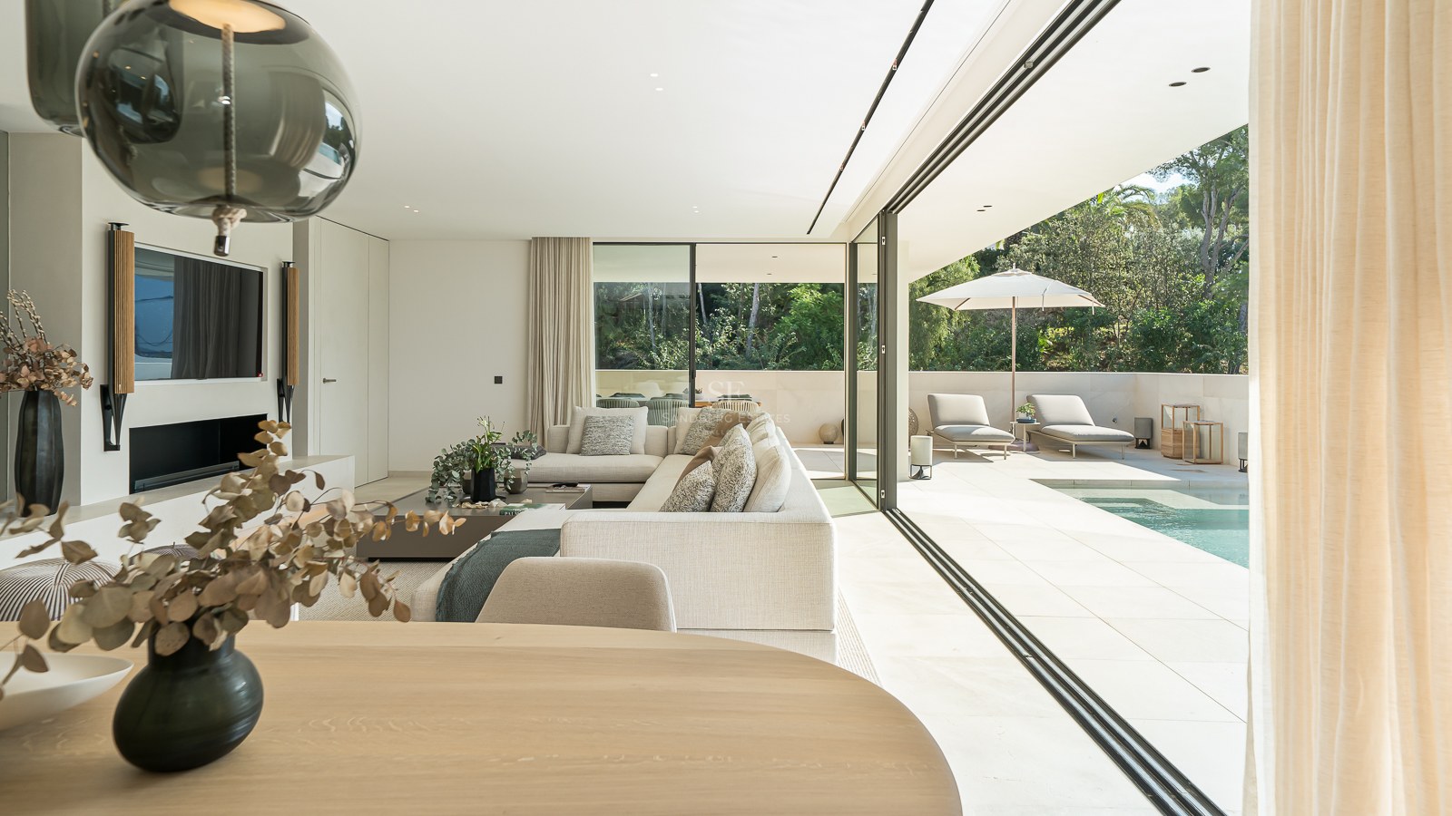 Salon moderne lumineux avec de grandes baies vitrées ouvrant sur une terrasse ensoleillée et une piscine privée.