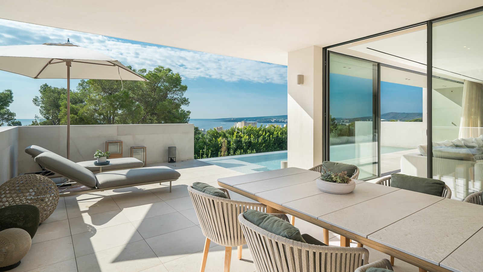 Terrasse moderne avec coin repas, chaises longues et piscine à débordement donnant sur la mer et la pinède.