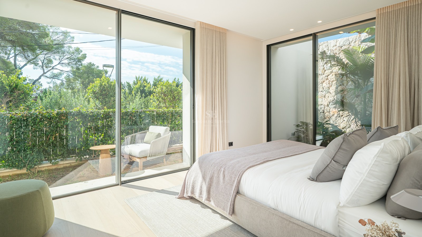 Chambre parentale lumineuse avec baies vitrées du sol au plafond donnant sur une terrasse privée verdoyante.
