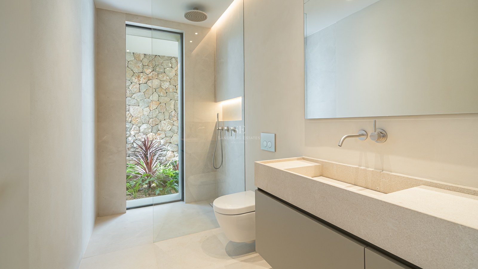 Salle de bain épurée avec double vasque en pierre, douche à l'italienne et fenêtre donnant sur un mur en pierre naturelle.