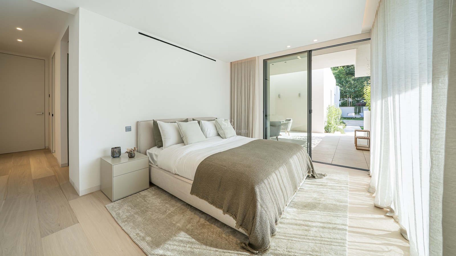 Chambre moderne avec grand lit, parquet clair et baies vitrées coulissantes ouvrant sur une terrasse privée.