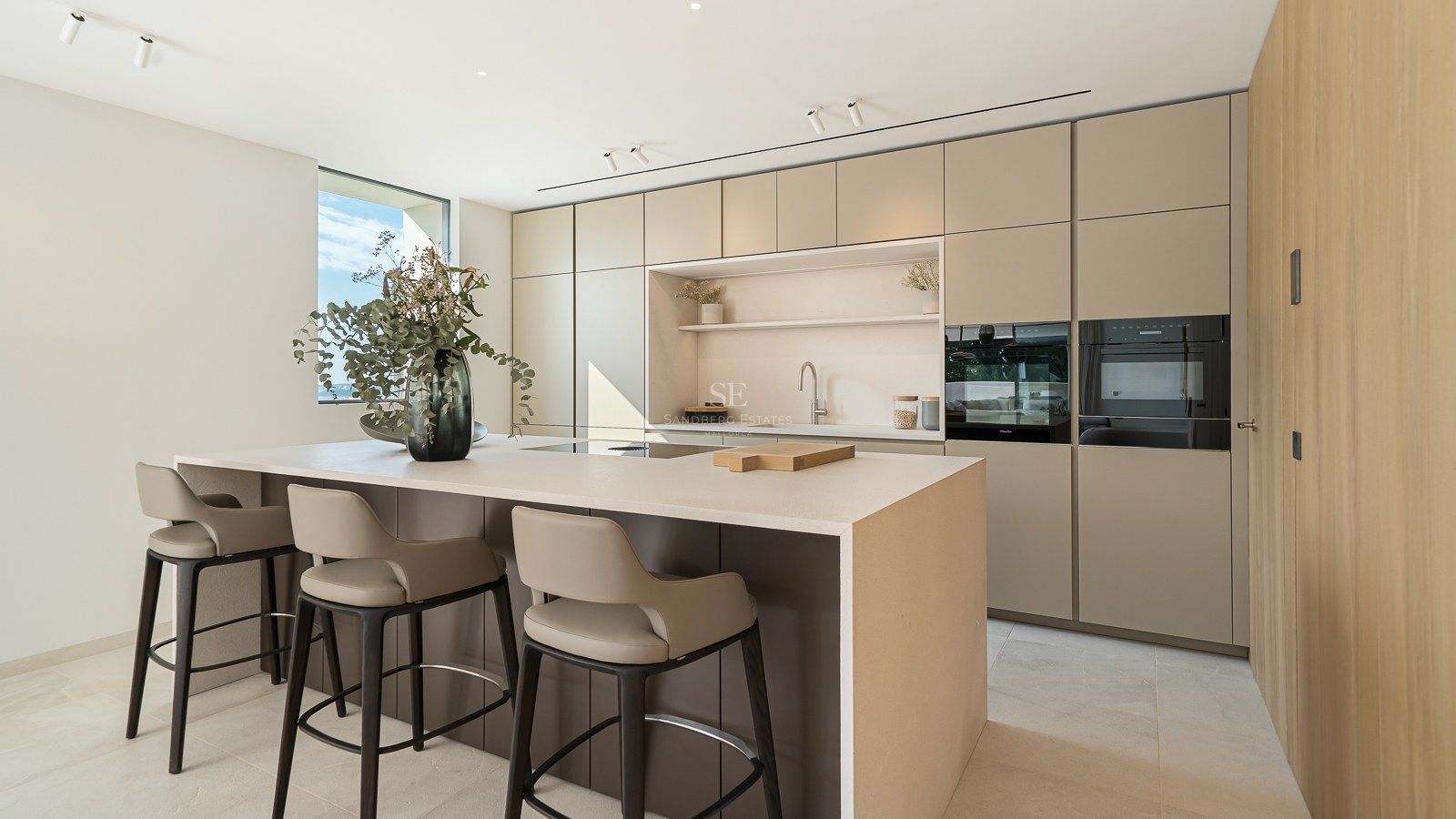 Cuisine moderne minimaliste avec un grand îlot central, des tabourets design et des armoires lisses aux tons terreux.