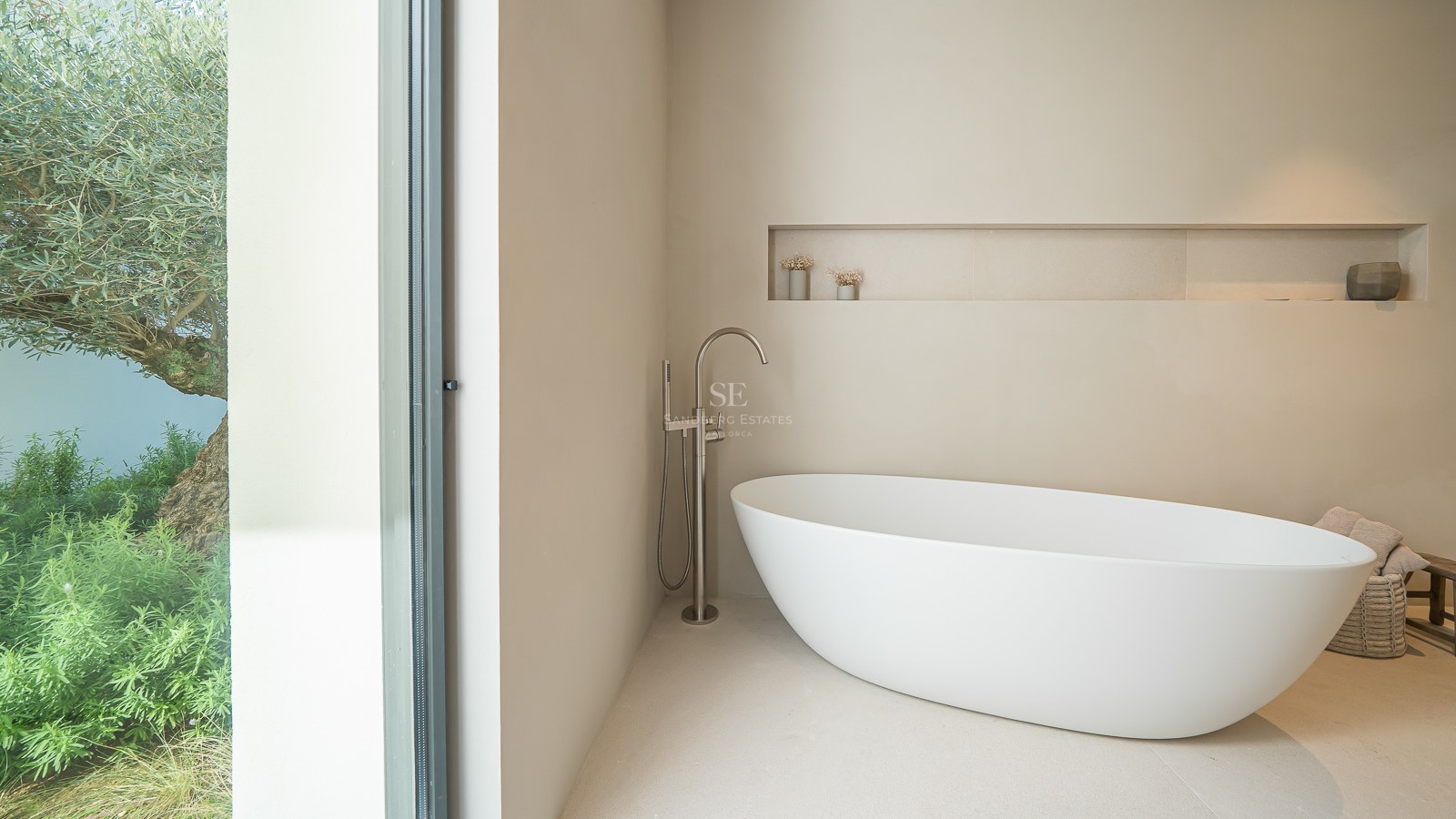 Salle de bain moderne avec baignoire îlot blanche et grande baie vitrée donnant sur un olivier.