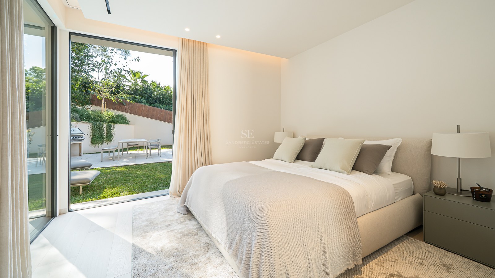Une chambre lumineuse avec un grand lit s'ouvrant sur un jardin privé par des baies vitrées coulissantes.