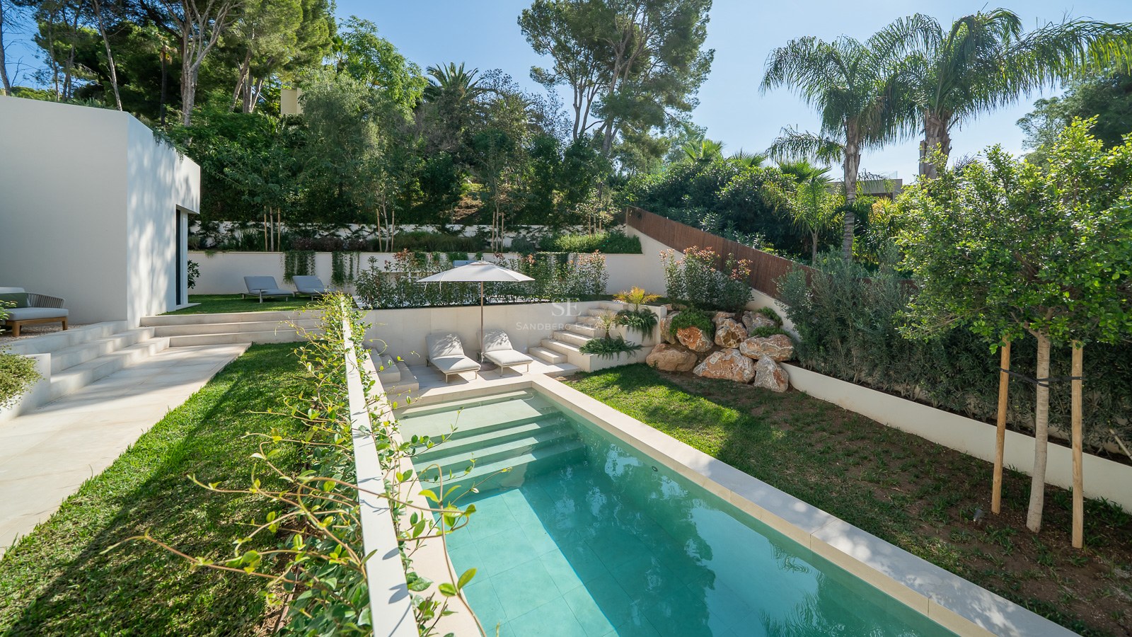 Piscine turquoise entourée d'une pelouse verdoyante, de murs blancs et d'une végétation luxuriante.