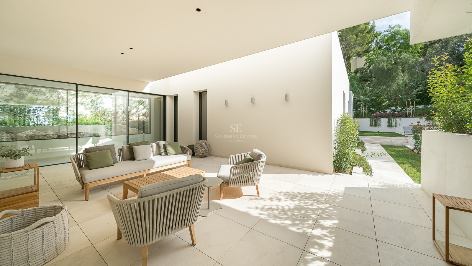 Terrasse de luxe avec canapé beige, coussins verts et chaises tressées sur un patio en pierre donnant sur le jardin.
