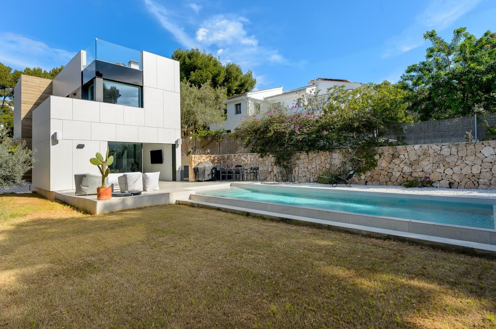 Villa blanca contemporánea con piscina rectangular, césped cuidado y muro perimetral de piedra natural bajo cielo despejado.