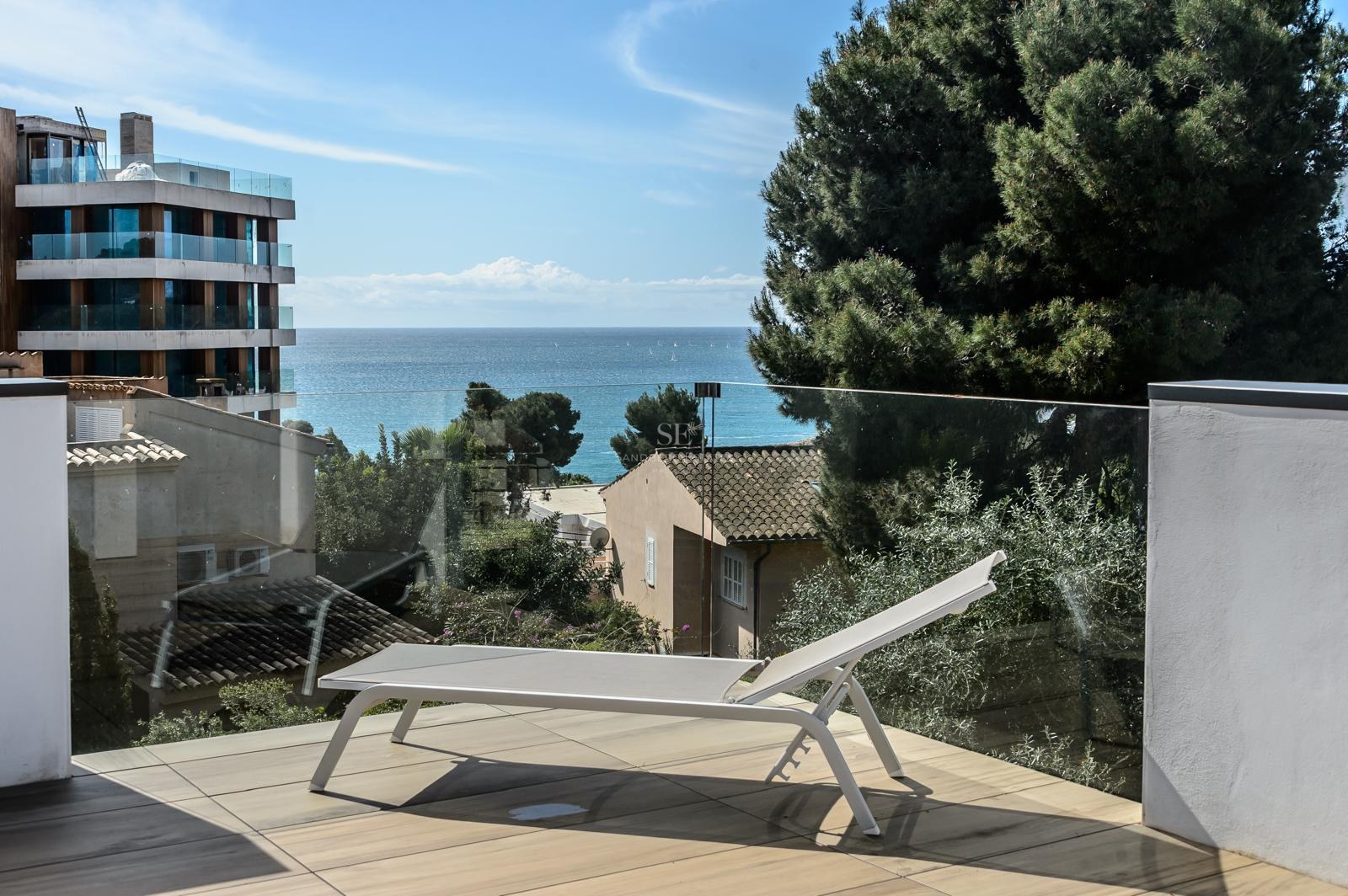 Tumbona blanca en terraza moderna con barandilla de cristal y vistas al mar Mediterráneo.