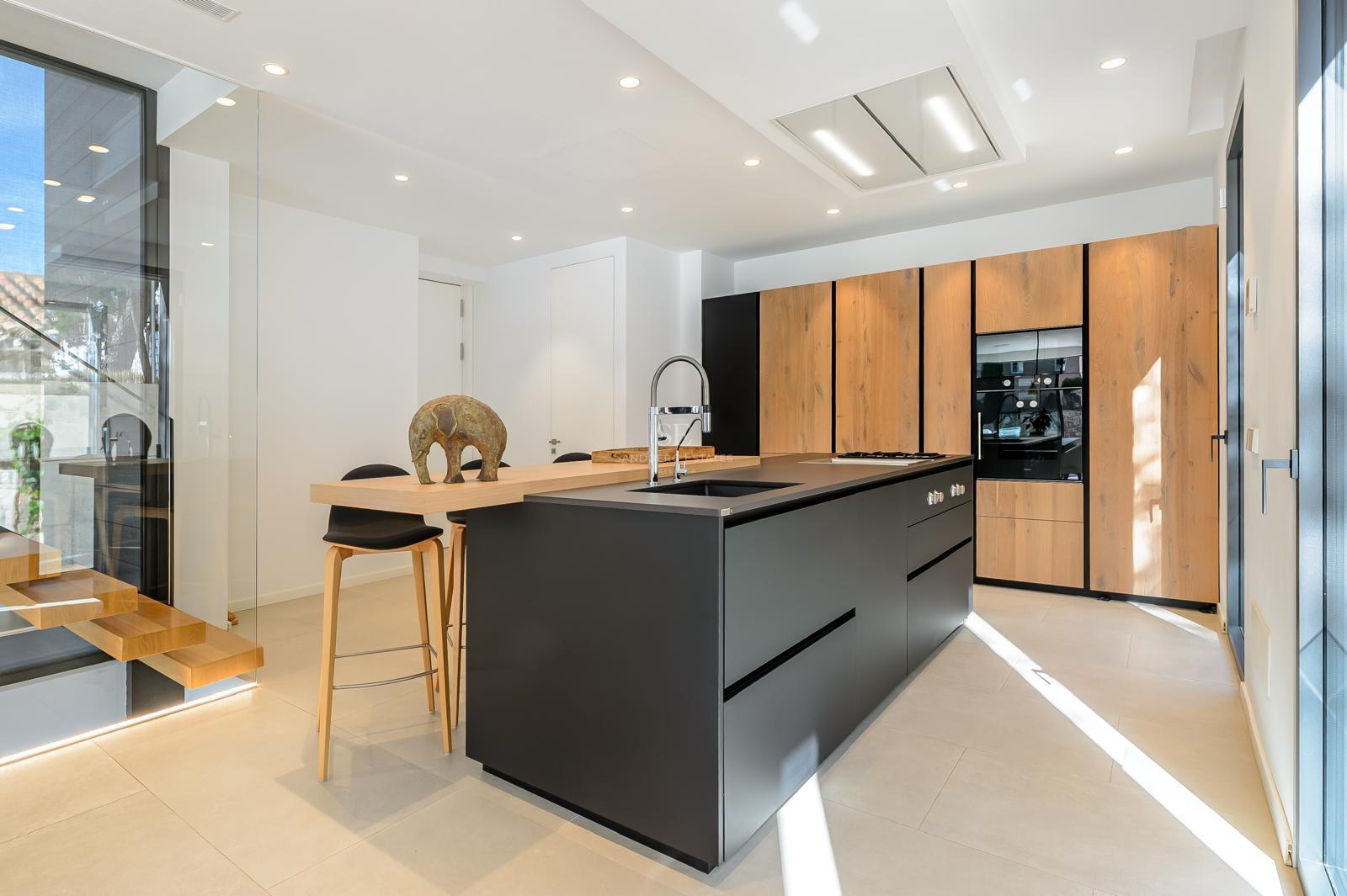 Cocina moderna con una gran isla negra, armarios de madera y electrodomésticos integrados bajo iluminación brillante.