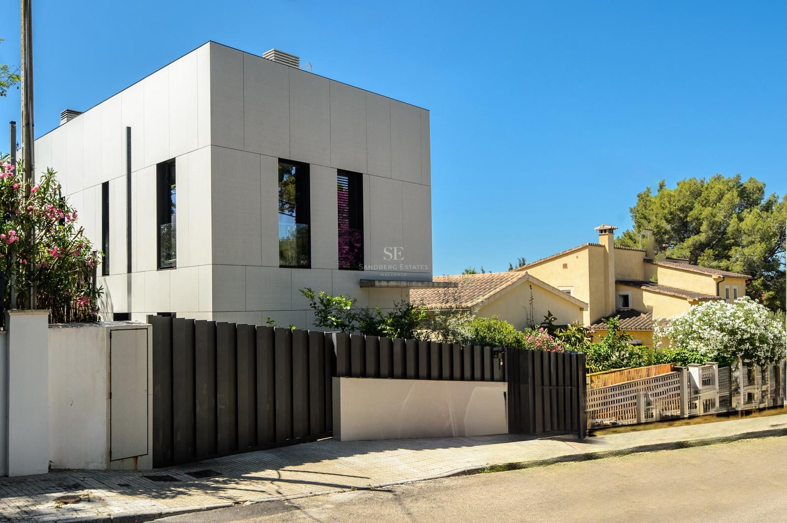 Exterior de una casa blanca de diseño moderno con valla negra y cielo azul despejado.